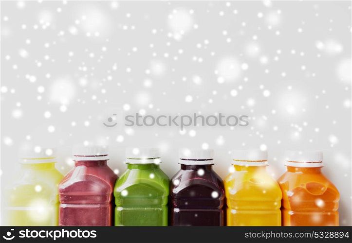 healthy eating, drinks, diet and detox concept - plastic bottles with different fruit or vegetable juices on white over snow. bottles with different fruit or vegetable juices