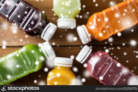 healthy eating, drinks, diet and packaging concept - close up of plastic bottles with different fruit or vegetable juices on wooden table over snow. bottles with different fruit or vegetable juices