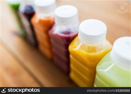 healthy eating, drinks, dieting and packaging concept - close up of plastic bottles with different fruit or vegetable juices on wooden table