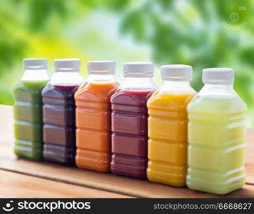 healthy eating, drinks, dieting and packaging concept - plastic bottles with different fruit or vegetable juices on wooden table over green natural background. bottles with different fruit or vegetable juices. bottles with different fruit or vegetable juices