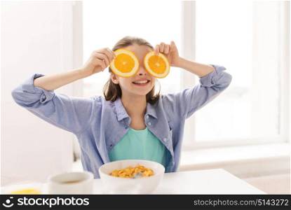 healthy eating, family and people concept - happy girl with orange slices having breakfast at home. happy girl with orange having breakfast at home
