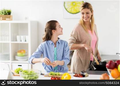 healthy eating, family and people concept - happy mother and daughter cooking vegetable salad and frying food for dinner at home kitchen. happy family cooking salad at home kitchen. happy family cooking salad at home kitchen