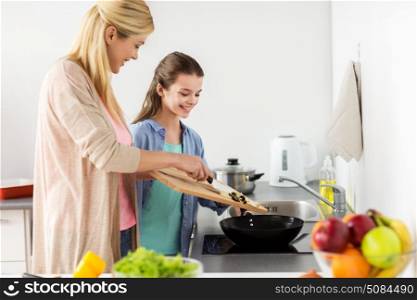 healthy eating, family and people concept - happy mother and daughter cooking and frying food for dinner at home kitchen. happy family cooking food at home kitchen. happy family cooking food at home kitchen