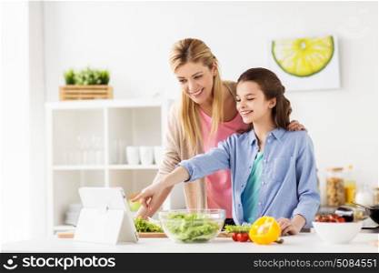 healthy eating, family and people concept - happy mother and daughter cooking vegetables for dinner using online recipe on tablet pc computer at home kitchen. family cooking dinner using tablet pc at kitchen. family cooking dinner using tablet pc at kitchen
