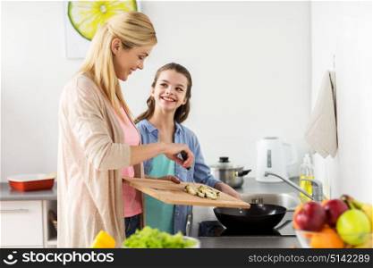 healthy eating, family and people concept - happy mother and daughter cooking and frying food for dinner at home kitchen. happy family cooking food at home kitchen