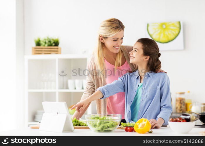 healthy eating, family and people concept - happy mother and daughter cooking vegetables for dinner using online recipe on tablet pc computer at home kitchen. family cooking dinner using tablet pc at kitchen