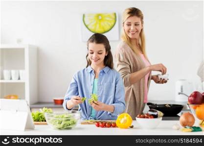 healthy eating, family and people concept - happy mother and daughter cooking vegetable salad and frying food for dinner at home kitchen. happy family cooking salad at home kitchen