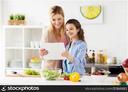 healthy eating, family and people concept - happy mother and daughter cooking vegetables for dinner using online recipe on tablet pc computer at home kitchen. family cooking dinner using tablet pc at kitchen