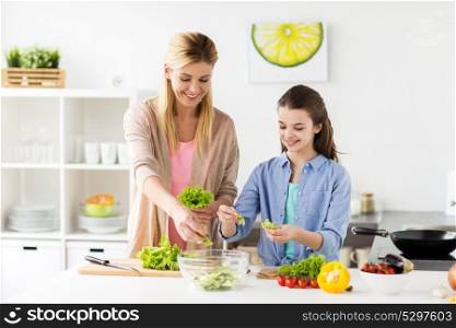 healthy eating, family and people concept - happy mother and daughter cooking vegetable salad for dinner at home kitchen. happy family cooking salad at home kitchen