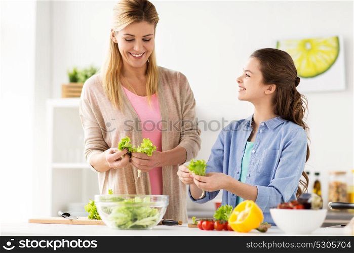 healthy eating, family and people concept - happy mother and daughter cooking vegetable salad for dinner at home kitchen. happy family cooking salad at home kitchen