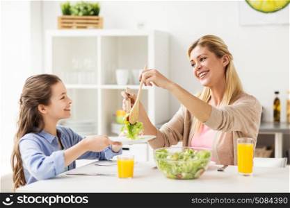 healthy eating, family and people concept - happy mother and daughter having vegetable salad for dinner at home kitchen. happy family eating salad at home kitchen. happy family eating salad at home kitchen