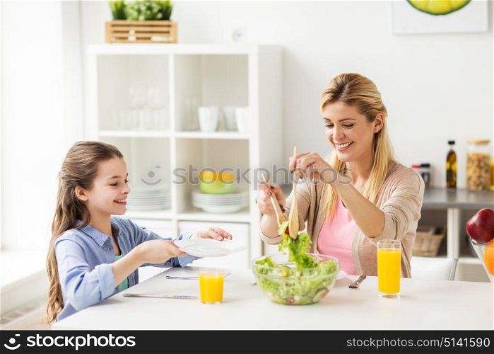 healthy eating, family and people concept - happy mother and daughter having vegetable salad for dinner at home kitchen. happy family eating salad at home kitchen