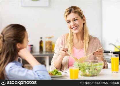 healthy eating, family and people concept - happy mother and daughter having vegetable salad for dinner at home kitchen. happy family eating salad at home kitchen