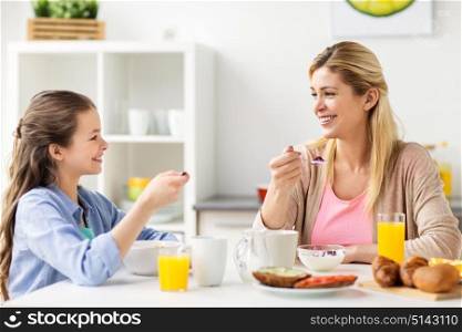 healthy eating, family and people concept - happy mother and daughter having breakfast at home kitchen. happy family having breakfast at home kitchen