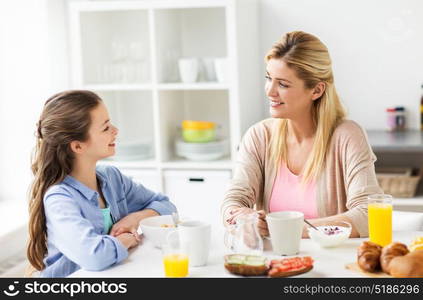 healthy eating, family and people concept - happy mother and daughter having breakfast at home kitchen. happy family having breakfast at home kitchen