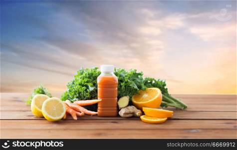 healthy eating, food and diet concept - bottle with carrot juice, fruits and vegetables on wooden table over sky background. bottle with carrot juice, fruits and vegetables. bottle with carrot juice, fruits and vegetables