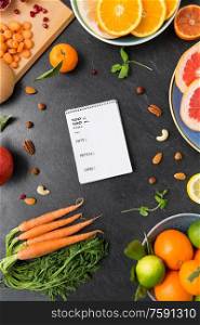 healthy eating, food and diet concept - close up of notebook, fruits and vegetables on slate table top with nutritional value. close up of notebook, fruits and vegetables