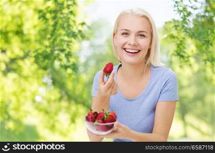 healthy eating, food and diet concept - happy smiling woman with strawberries over green natural background. happy smiling woman eating strawberry