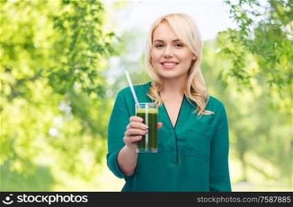 healthy eating, food and diet concept - happy smiling young woman drinking green vegetable juice or smoothie from glass over green natural background. smiling woman drinking vegetable juice or smoothie
