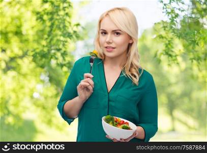 healthy eating, food and diet concept - happy smiling young woman eating vegetable salad with fork over green natural background. smiling young woman eating vegetable salad