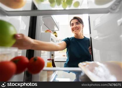 healthy eating, food and diet concept - happy woman taking apple from fridge at home kitchen. happy woman taking food from fridge at home