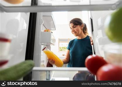 healthy eating, food and diet concept - happy woman taking bottle of orange juice from fridge at home kitchen. happy woman taking juice from fridge at home