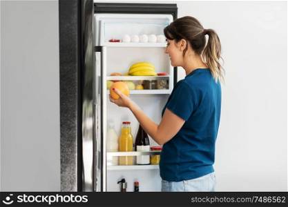 healthy eating, food and diet concept - happy woman taking grapefruit from fridge at home kitchen. happy woman taking food from fridge at home