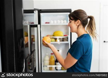 healthy eating, food and diet concept - happy woman taking grapefruit from fridge at home kitchen. happy woman taking food from fridge at home