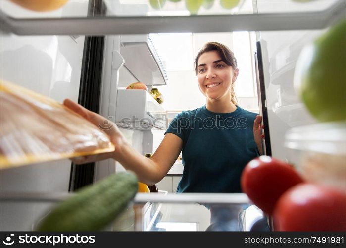 healthy eating, food and diet concept - happy woman taking meat from fridge at home kitchen. happy woman taking food from fridge at home