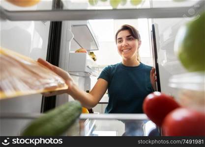 healthy eating, food and diet concept - happy woman taking meat from fridge at home kitchen. happy woman taking food from fridge at home