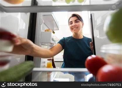 healthy eating, food and diet concept - happy woman taking yoghurt from fridge at home kitchen. happy woman taking food from fridge at home