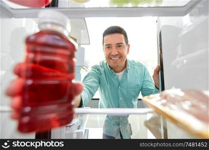 healthy eating, food and diet concept - middle-aged man taking bottle of juice from fridge at home kitchen. man taking juice from fridge at home kitchen