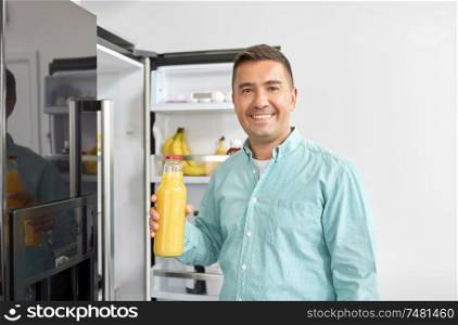 healthy eating, food and diet concept - middle-aged man taking bottle of orange juice from fridge at home kitchen. man taking juice from fridge at home kitchen