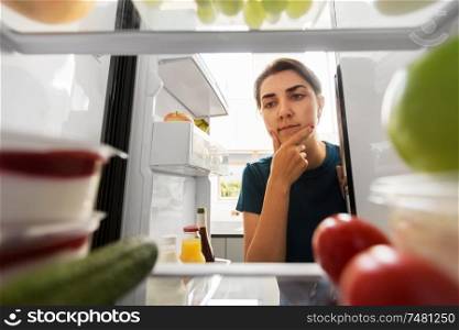 healthy eating, food and diet concept - thoughtful woman at open fridge at home kitchen. thoughtful woman at open fridge at home kitchen