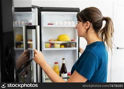 healthy eating, food and diet concept - woman at open fridge at home kitchen. woman at open fridge at home kitchen
