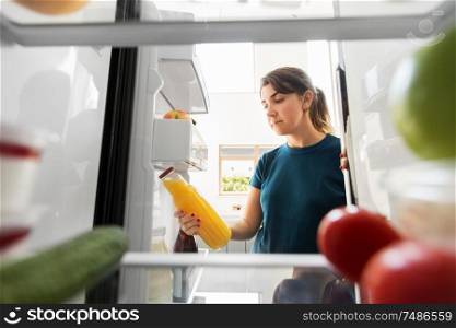 healthy eating, food and diet concept - woman taking bottle of orange juice from fridge at home kitchen. woman taking bottle of juice from fridge at home