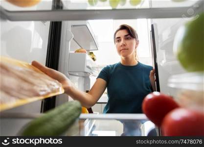 healthy eating, food and diet concept - woman taking meat from fridge at home kitchen. woman taking food from fridge at home