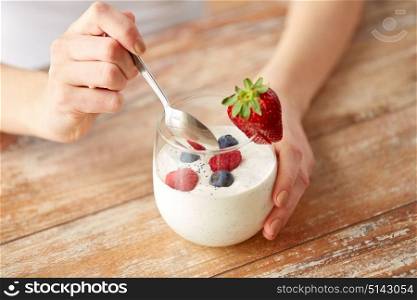healthy eating, food and people concept - close up of woman hands with yogurt and berries in glass on table. woman hands with yogurt and berries on table