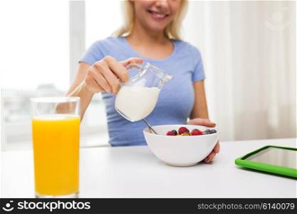 healthy eating, food and people concept - close up of woman pouring milk from jug to bowl with breakfast at home