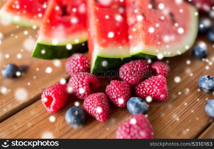 healthy eating, food and vegetarian concept - close up of raspberry, blackberry and watermelon slices on wooden table over snow. close up of fruits and berries on wooden table