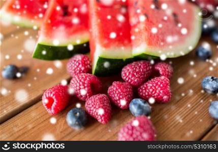 healthy eating, food and vegetarian concept - close up of raspberry, blackberry and watermelon slices on wooden table over snow. close up of fruits and berries on wooden table