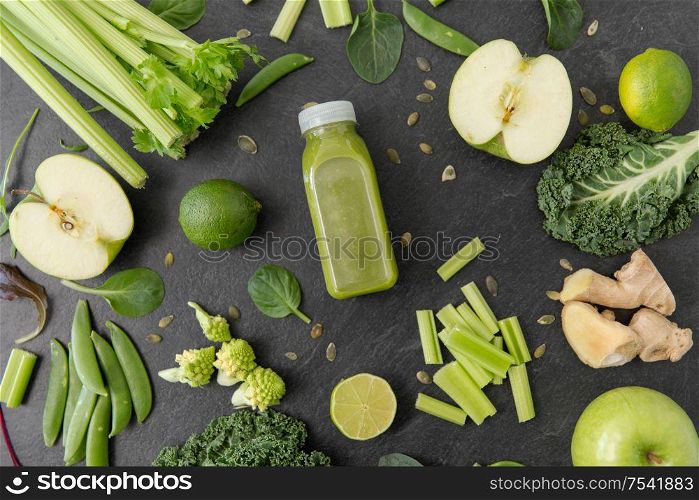 healthy eating, food and vegetarian diet concept - bottle of fresh green juice or smoothie, fruits and vegetables on slate stone background. close up of bottle with green juice and vegetables