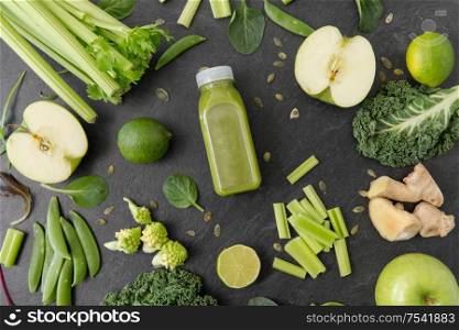 healthy eating, food and vegetarian diet concept - bottle of fresh green juice or smoothie, fruits and vegetables on slate stone background. close up of bottle with green juice and vegetables