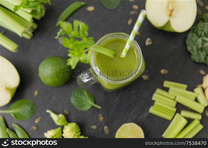 healthy eating, food and vegetarian diet concept - close up of glass mug with fresh green juice or smoothie, fruits and vegetables on slate stone background. close up of glass mug with green vegetable juice