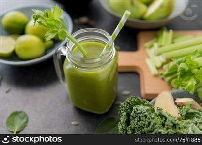 healthy eating, food and vegetarian diet concept - close up of glass mug of fresh green juice or smoothie with paper straw, fruits and vegetables on slate stone background. close up of glass mug with green vegetable juice