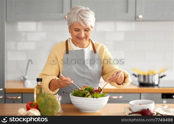 healthy eating, food cooking and culinary concept - happy smiling senior woman making vegetable salad on kitchen at home. happy woman cooking salad on kitchen at home