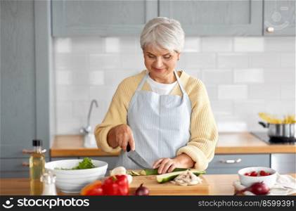 healthy eating, food cooking and culinary concept - happy smiling senior woman with knife chopping zucchini on kitchen at home. happy woman chopping zucchini on kitchen