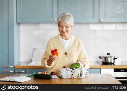 healthy eating, food cooking and culinary concept - happy smiling woman with vegetables in string bag and cook book on kitchen. woman with vegetables and cook book on kitchen