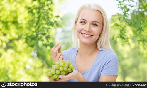 healthy eating, food, diet and people concept - happy smiling woman eating grapes over green natural background. happy woman eating grapes