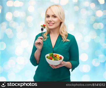 healthy eating, food, diet and people concept - smiling young woman eating vegetable salad with fork over blue holidays lights background